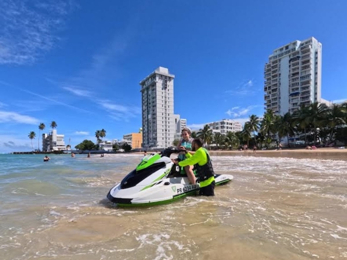 Person on a green and white jet ski near a sandy beach and tall buildings.