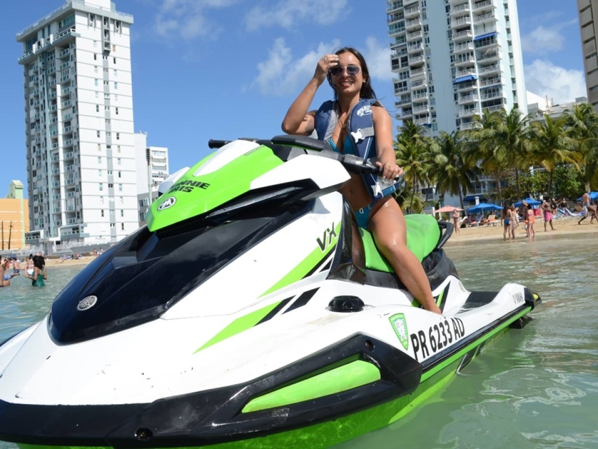 Person on a green and white jet ski near a beach with city buildings in the background.