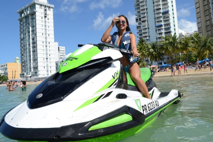 Person on a green and white jet ski near a beach with city buildings in the background.