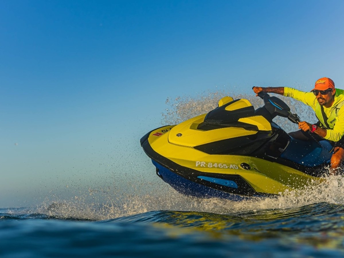 Person riding a yellow jet ski on the water with a clear blue sky.