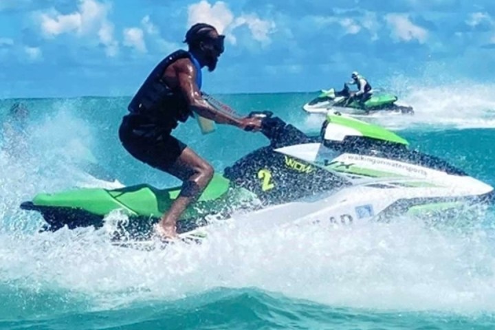 Three people riding jet skis in turquoise ocean under blue sky.