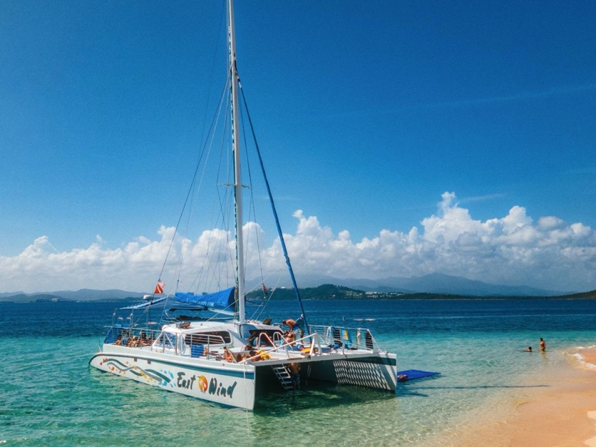 Catamaran on beach with people and clear blue sky.