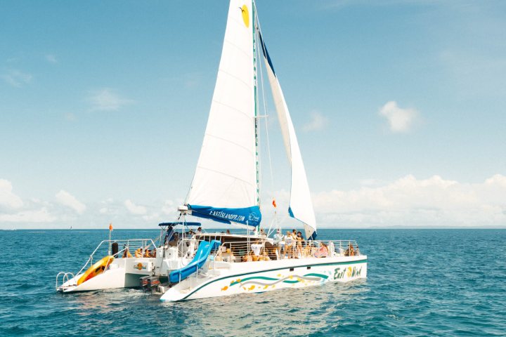 Catamaran with sails on the ocean under a clear sky.