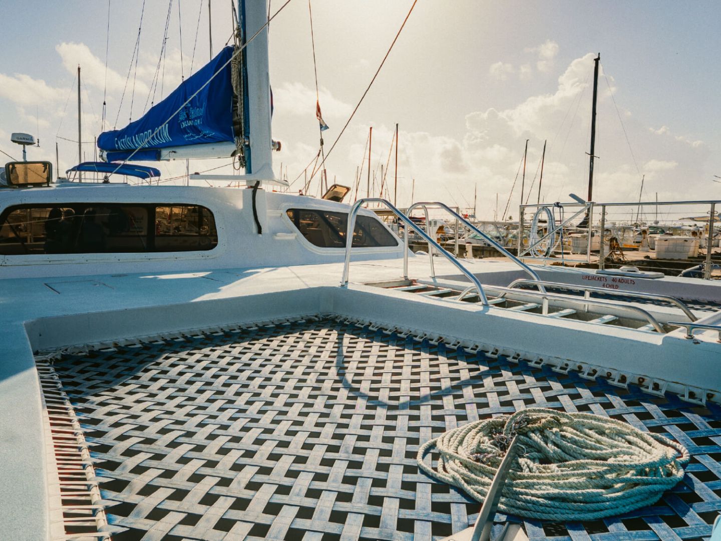 Catamaran deck with netting, coiled rope, and marina view.