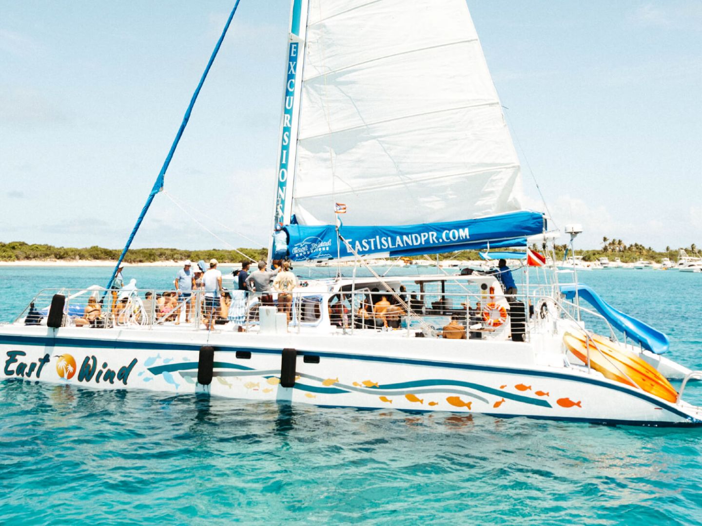 Sailing catamaran with tourists on clear blue water near a tropical island.