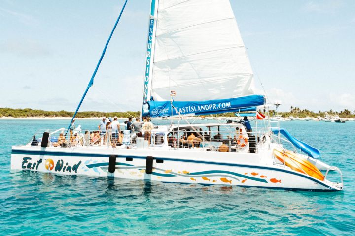 Sailing catamaran with tourists on clear blue water near a tropical island.