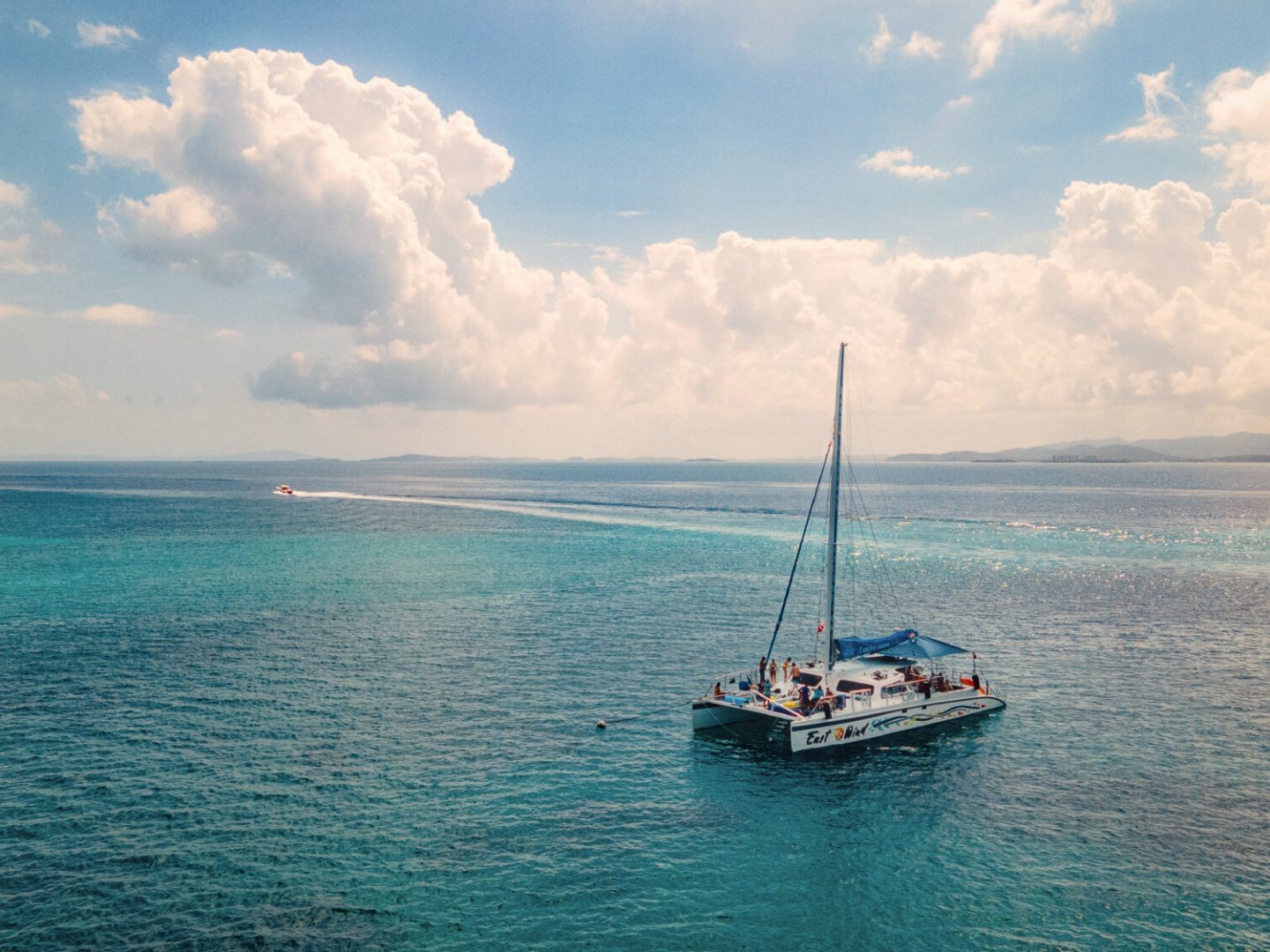 Catamaran sailing on clear blue ocean under a partly cloudy sky.