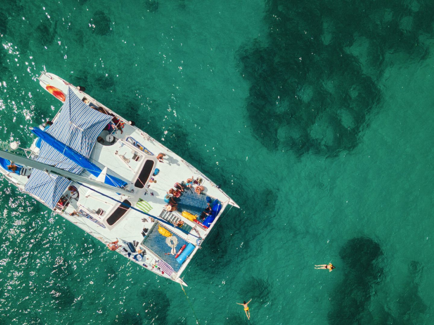 Aerial view of a catamaran on turquoise water with swimmers nearby.