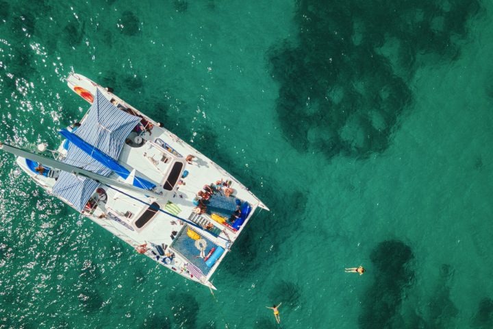 Aerial view of a catamaran on turquoise water with swimmers nearby.