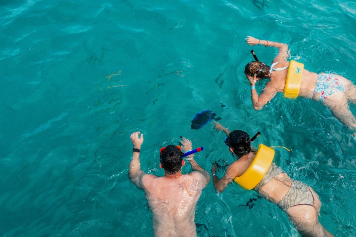 Three people snorkeling in clear blue water with snorkeling gear and life vests.